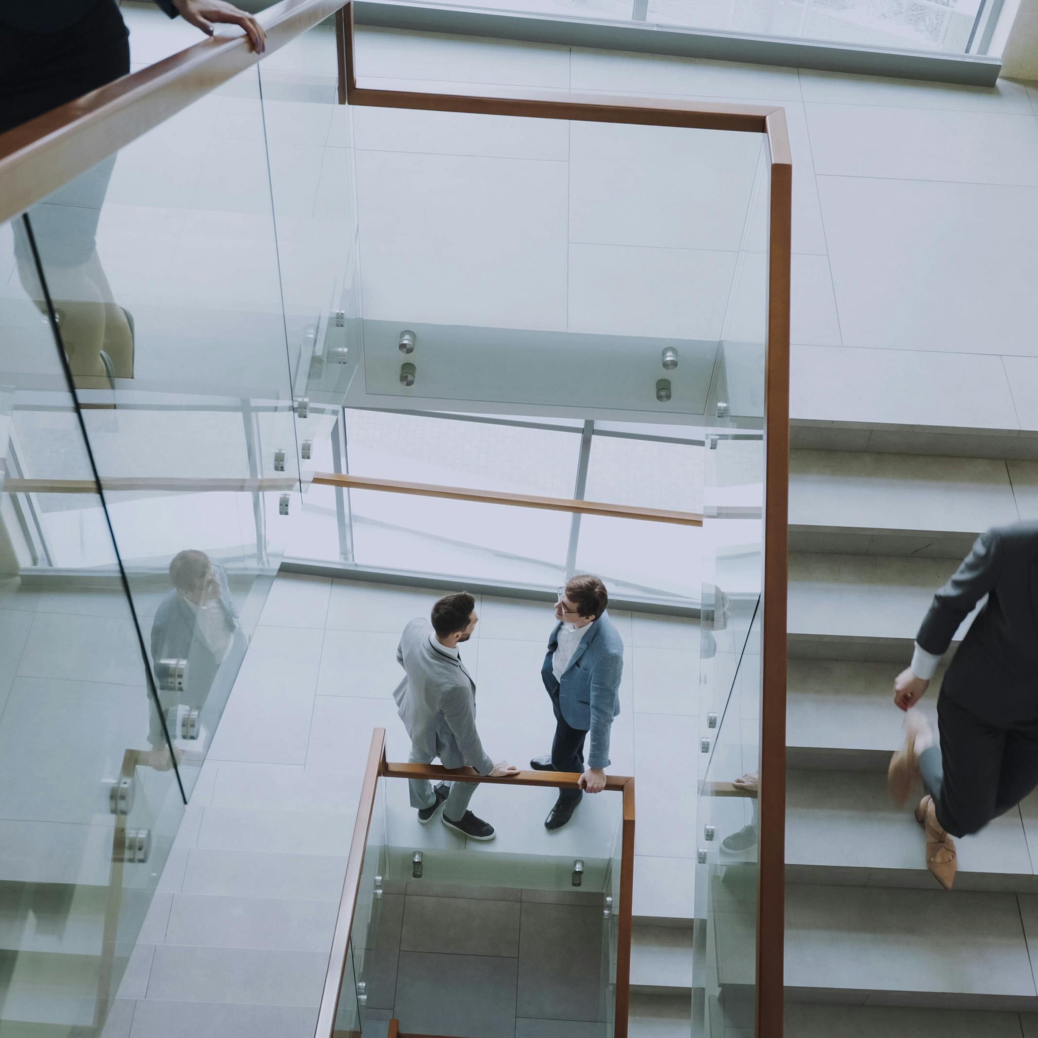 Aerial view of professionals conversing in a glass staircase in a modern office.