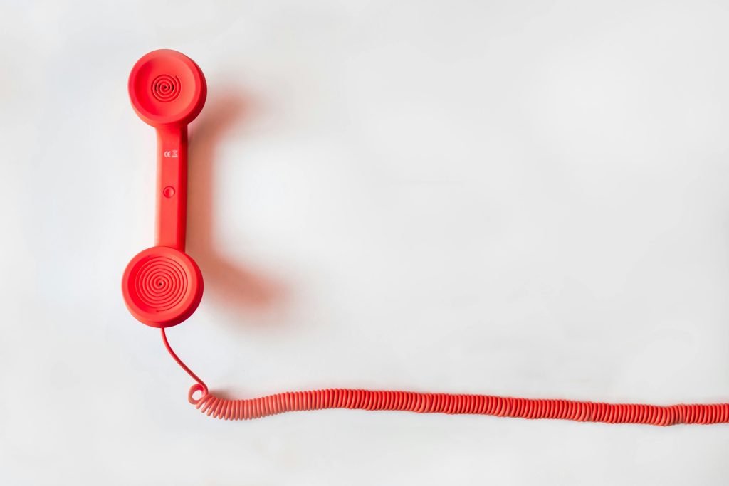 Usluge Vintage red phone handset with coiled cable on a clean white background, classic communication device.